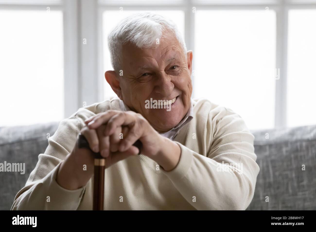 Positive old grandfather holding walking stick resting on couch Stock Photo
