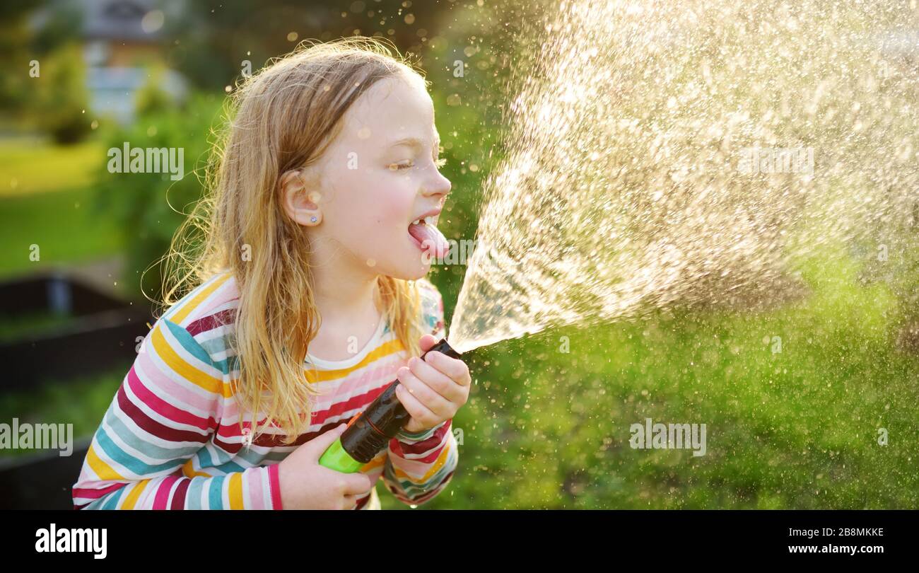Adorable little girl playing with a garden hose on warm summer day