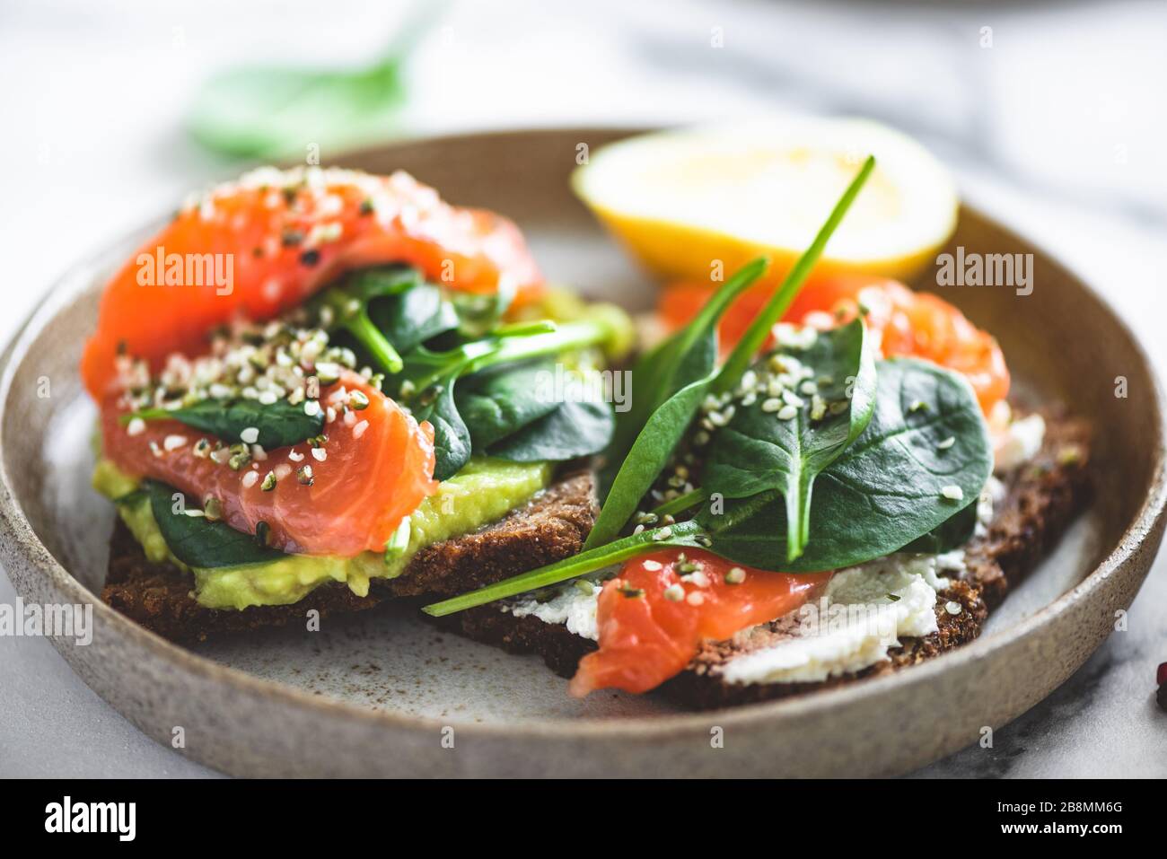 Rye bread toast with avocado, salmon, cream cheese, spinach leaf and hemp seeds on plate