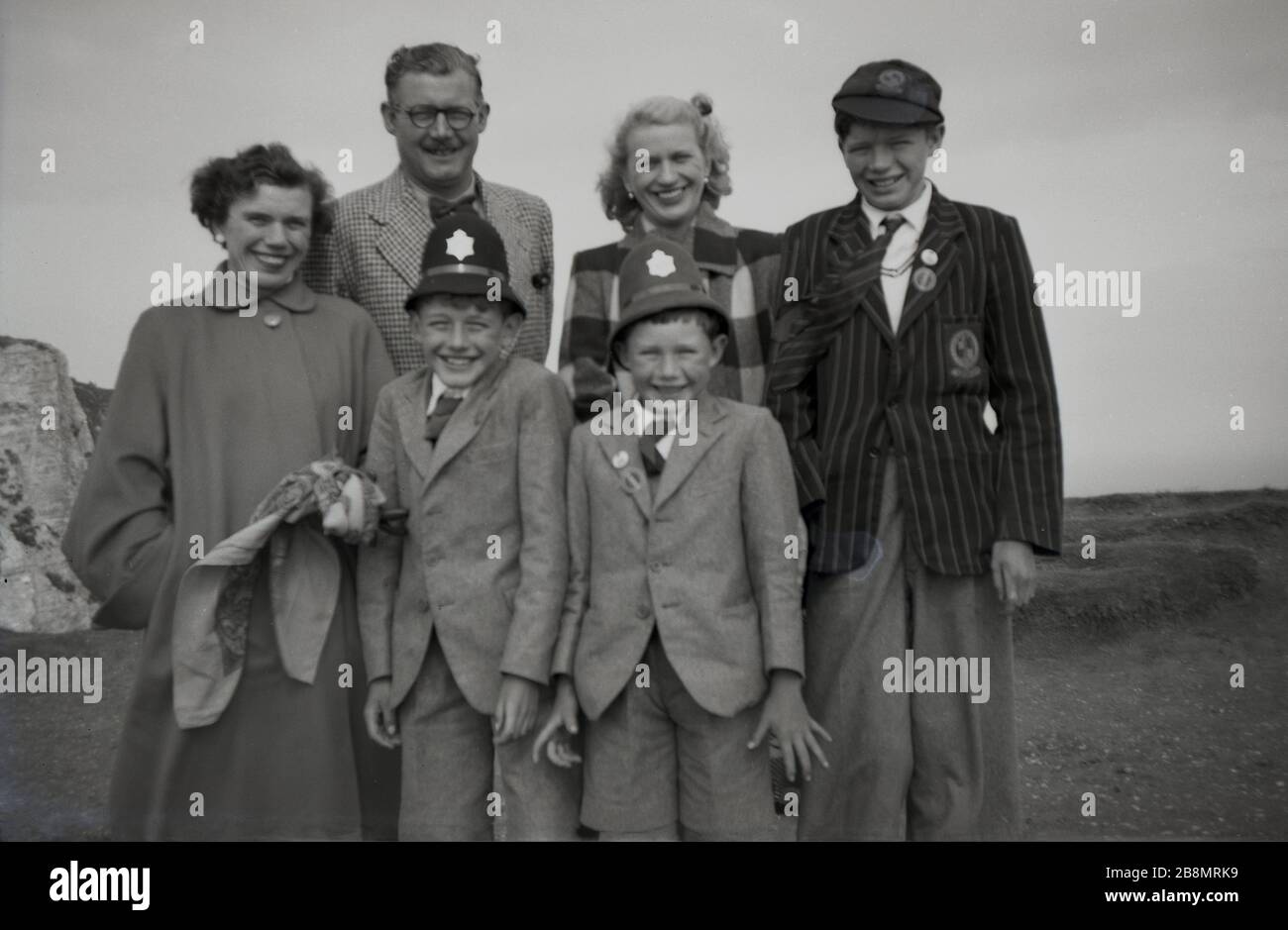 1952, historical, family photo, mum, dad and three boys in their school uniform, with the two youngest having fun wearing their imitation or fancy dress police helmets, England, UK. Stock Photo