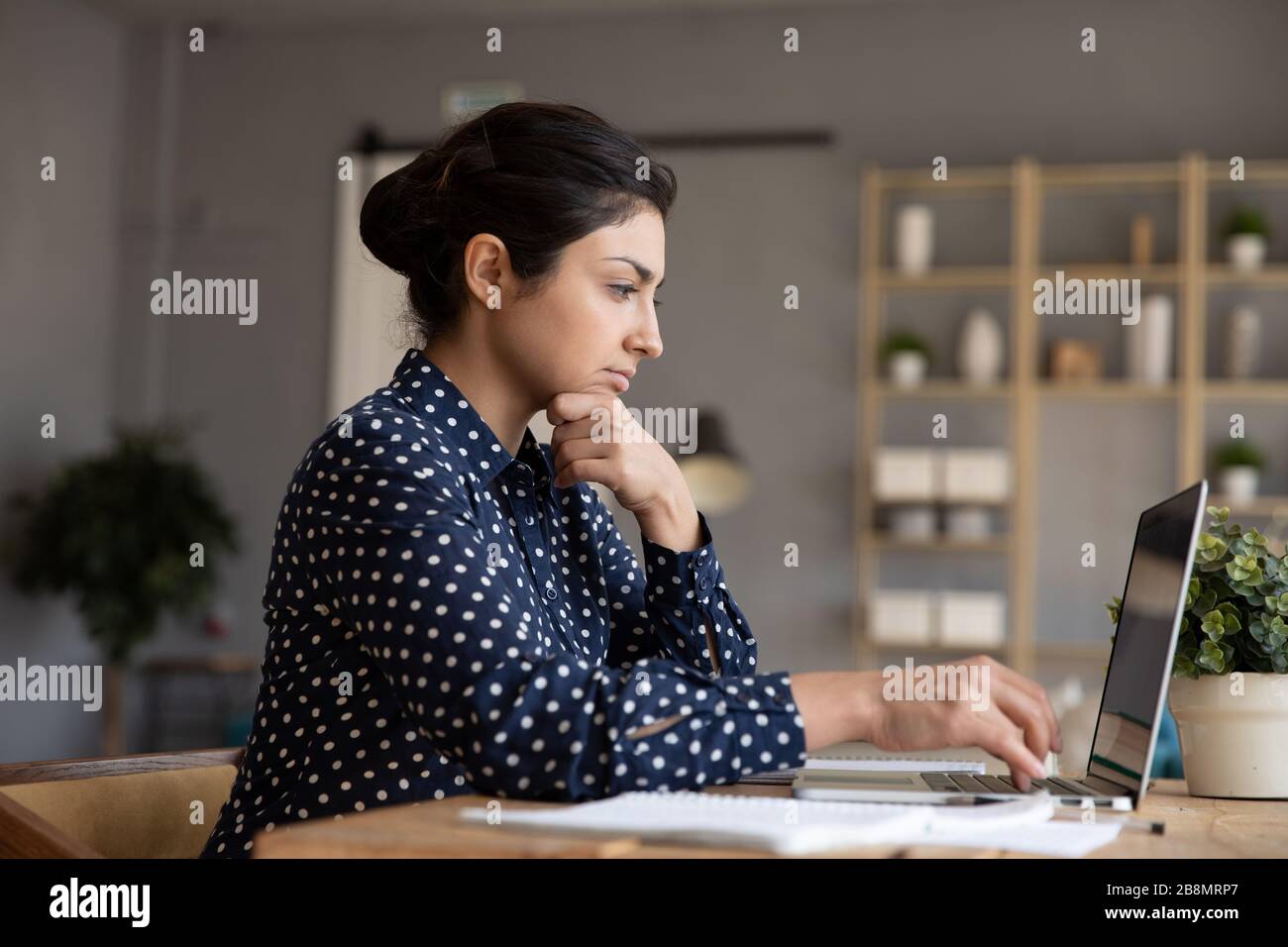 Thoughtful Indian woman looking at laptop screen, pondering task Stock Photo