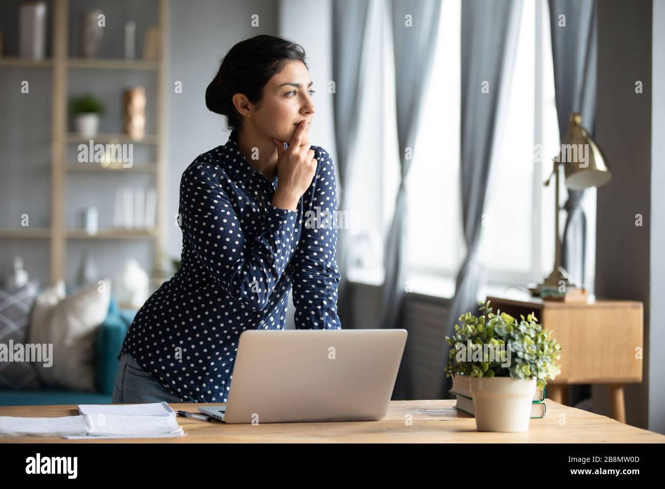 Thoughtful Indian woman standing at desk, pondering task Stock Photo