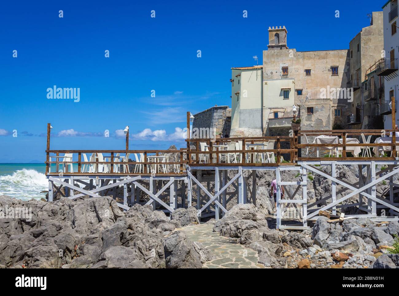 Wooden pier over path on a rocky shore in Cefalu city, located on the Tyrrhenian coast of Sicily, Italy - view with Chiesa Santa Maria dell Itria Stock Photo