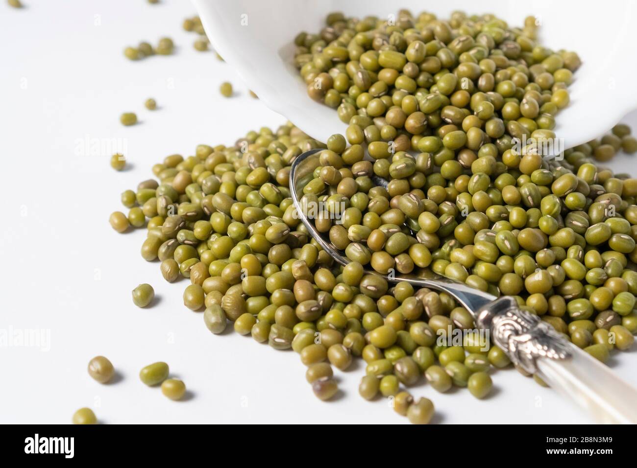 Heap of green mung beans in a white ceramic bowl on a white table close-up Stock Photo