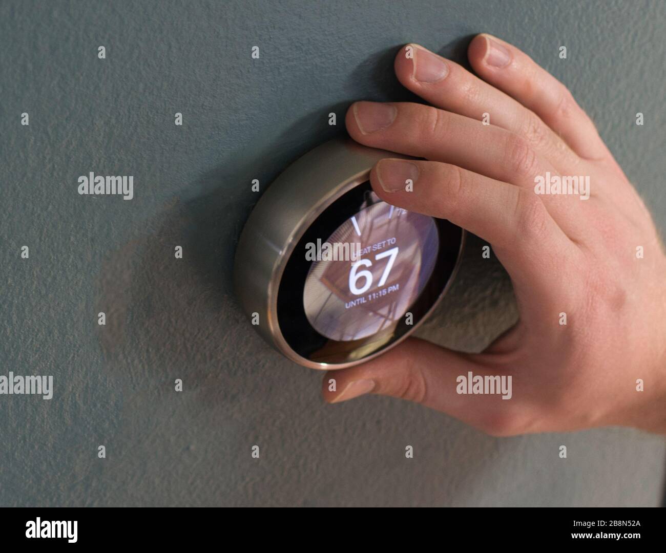 Hand adjusting the dial on smart home thermostat. Pressing center button to save money heating and cooling. Stock Photo