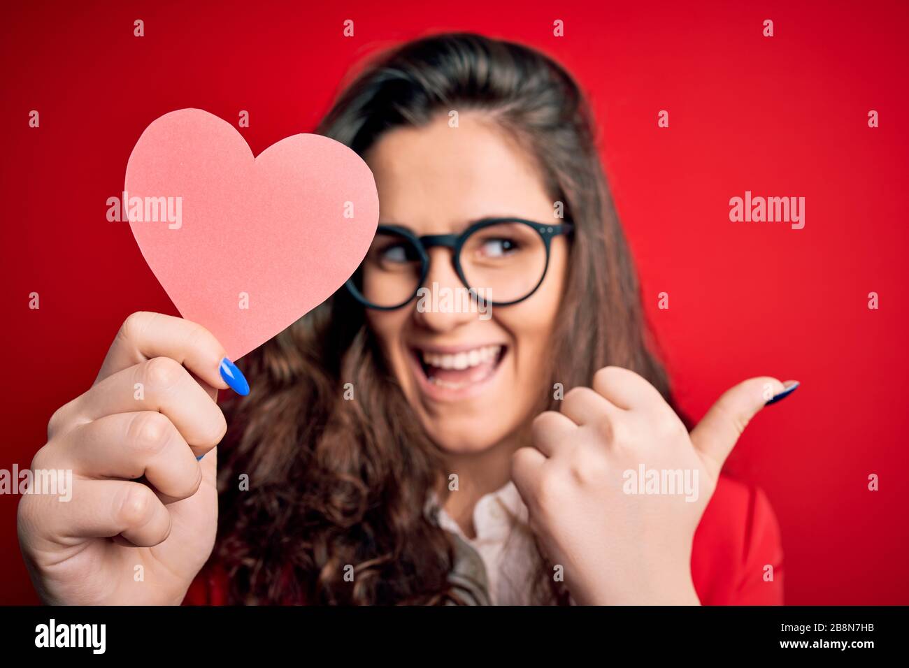 Young beautiful woman with curly hair holding paper heart over isolated ...