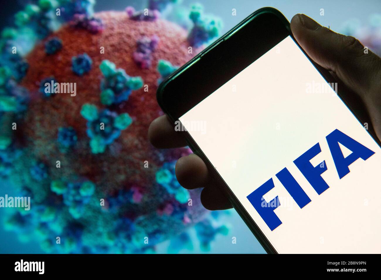 China. 20th Mar, 2020. In this photo illustration the Fédération Internationale de Football Association (FIFA) logo seen displayed on a smartphone with a computer model of the COVID-19 coronavirus on the background. Credit: Budrul Chukrut/SOPA Images/ZUMA Wire/Alamy Live News Stock Photo