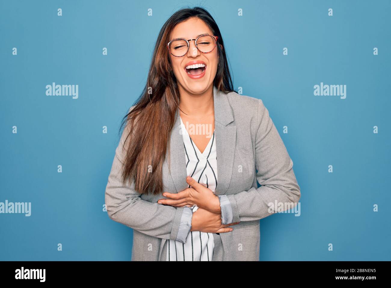 Young hispanic business woman wearing glasses standing over blue ...