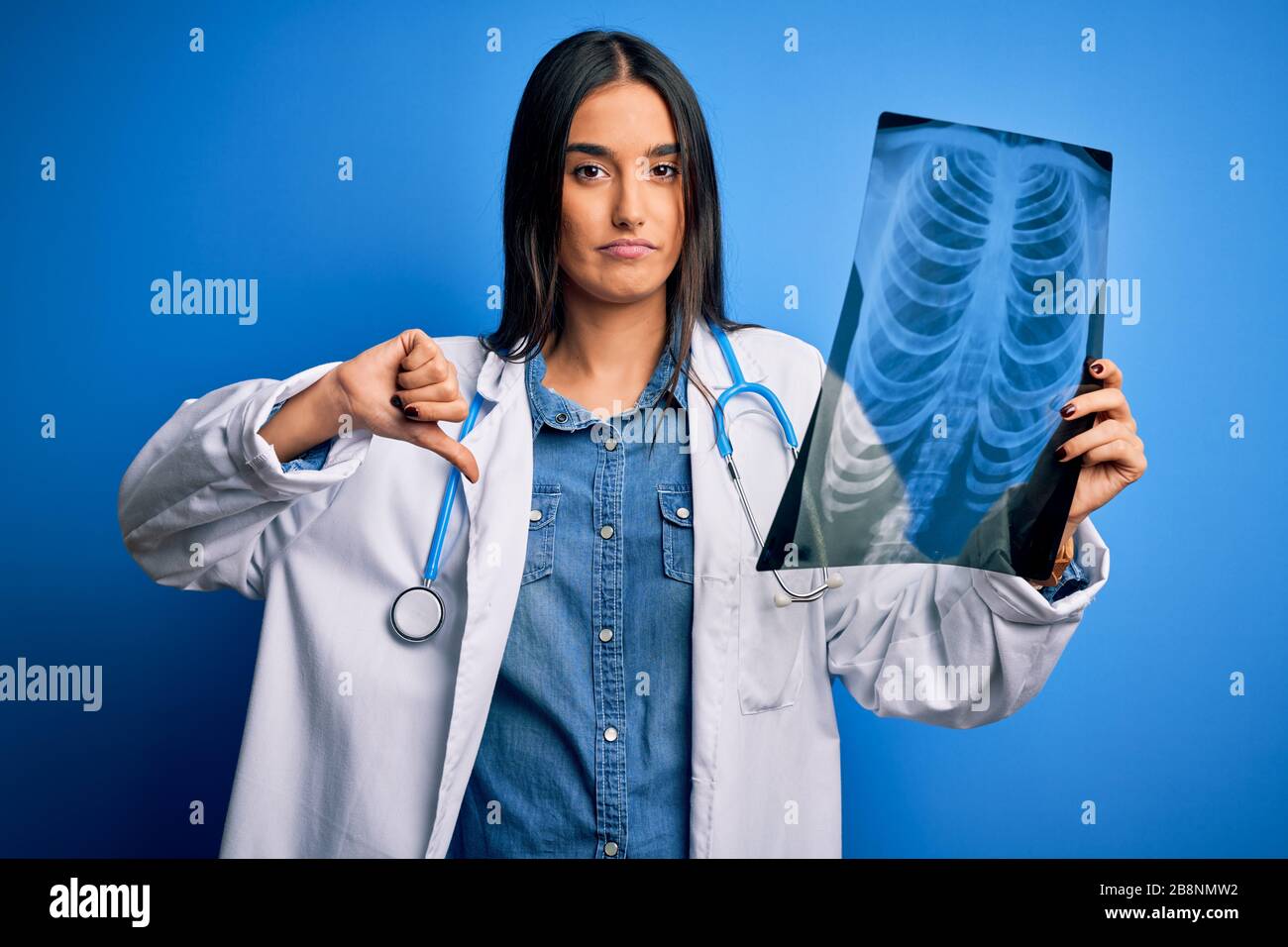 Young beautiful brunette doctor woman wearing stethoscope holding chest ...