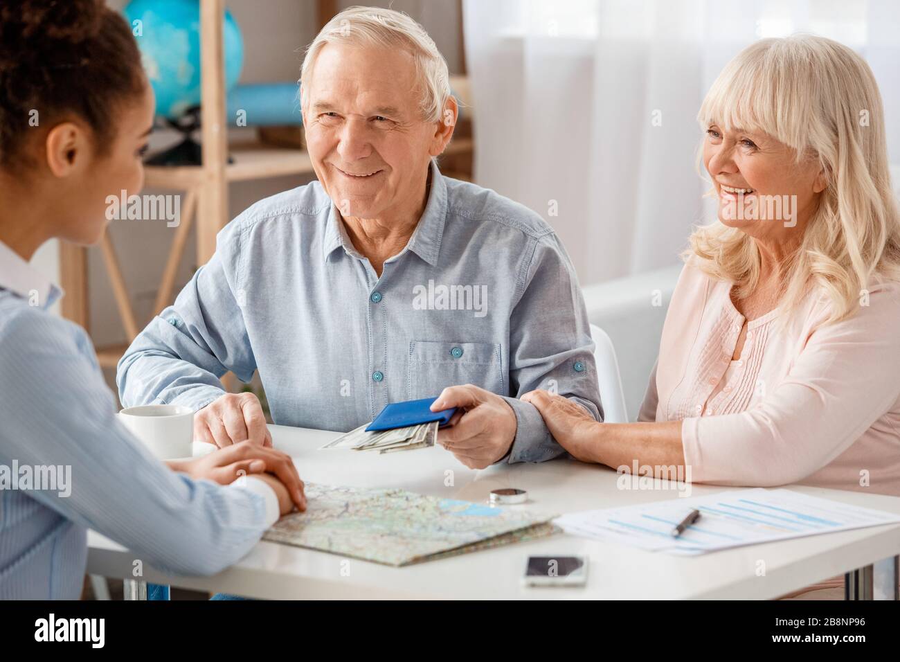 Travel agent at office sitting with senior clients man givving passport and money smiling happy Stock Photo