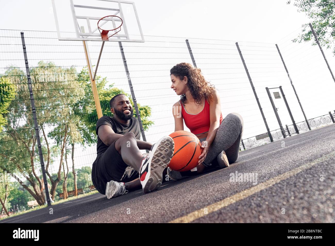 Outdoors Activity. African couple sitting with ball on basketball court talking laughing cheerful Stock Photo