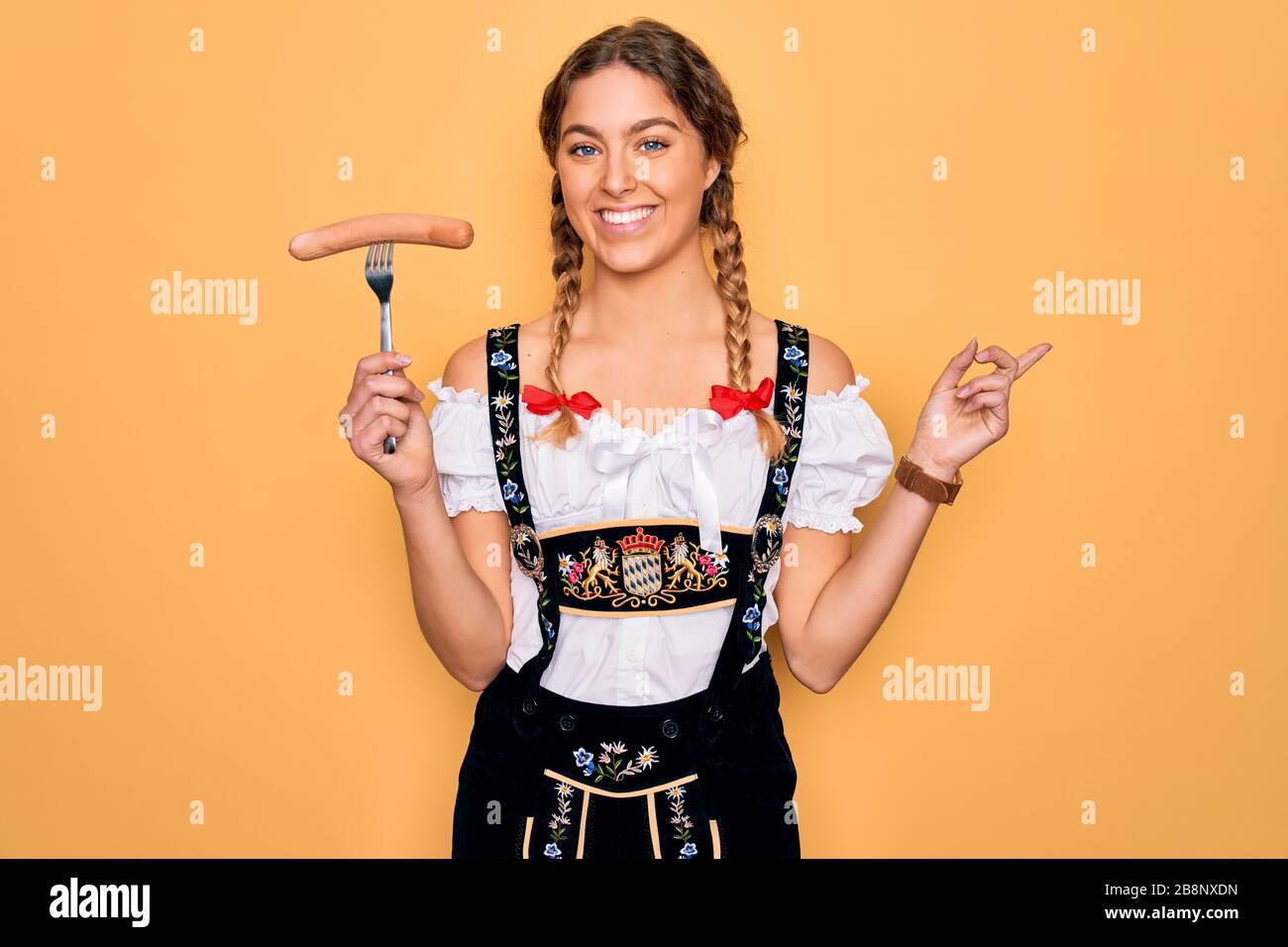 Beautiful german woman with blue eyes wearing oktoberfest dress holding  fork with sausage very happy pointing with hand and finger to the side  Stock Photo - Alamy
