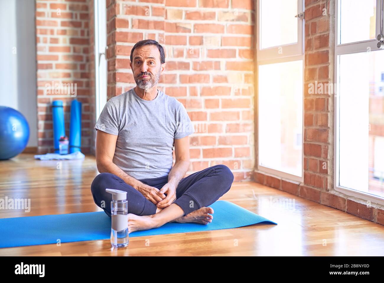 Middle age handsome sportman sitting on mat doing stretching yoga exercise at gym puffing cheeks with funny face. Mouth inflated with air crazy expre Stock Photo Alamy