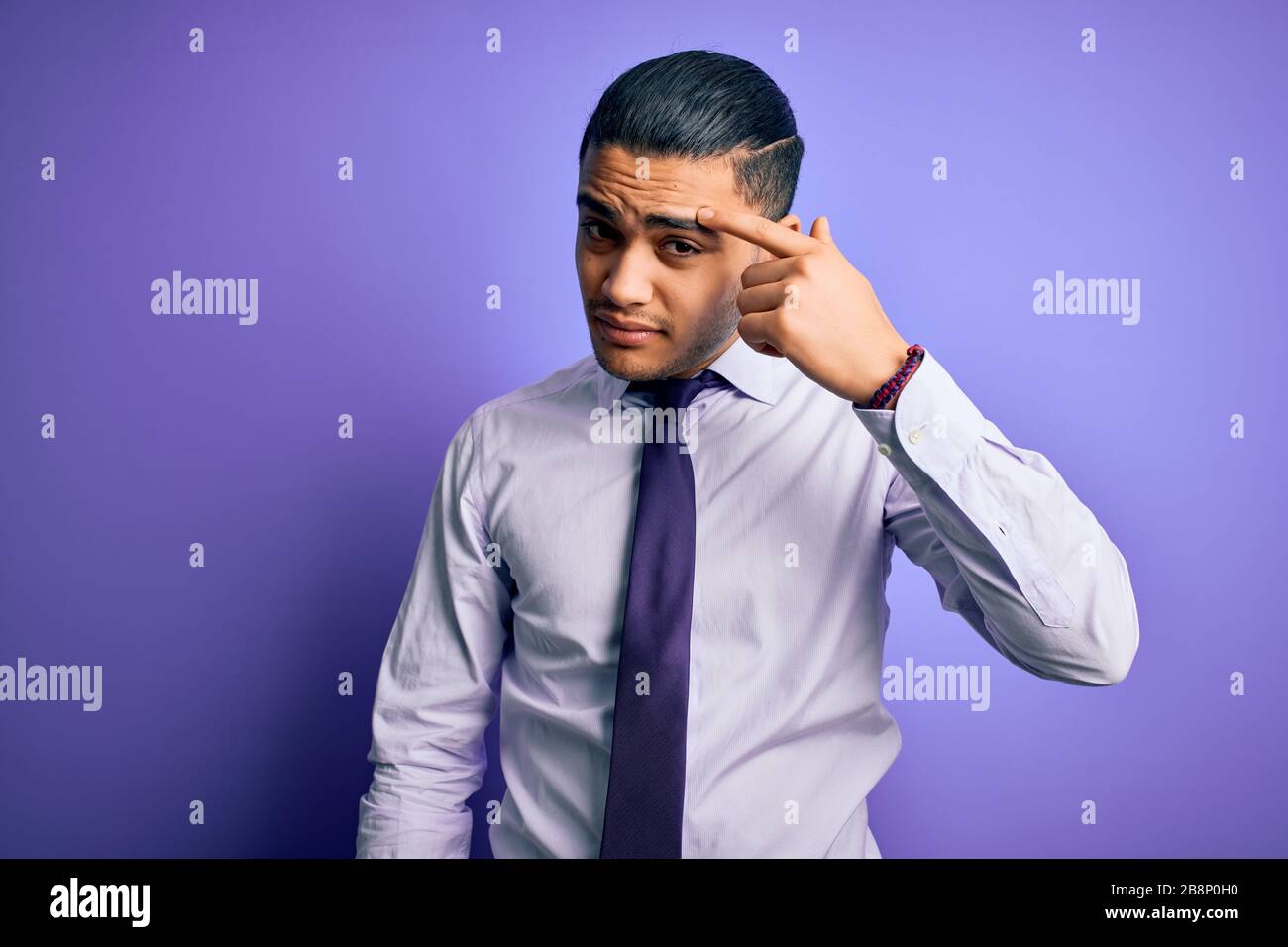 Young brazilian businessman wearing elegant tie standing over isolated purple background pointing unhappy to pimple on forehead, ugly infection of bla Stock Photo