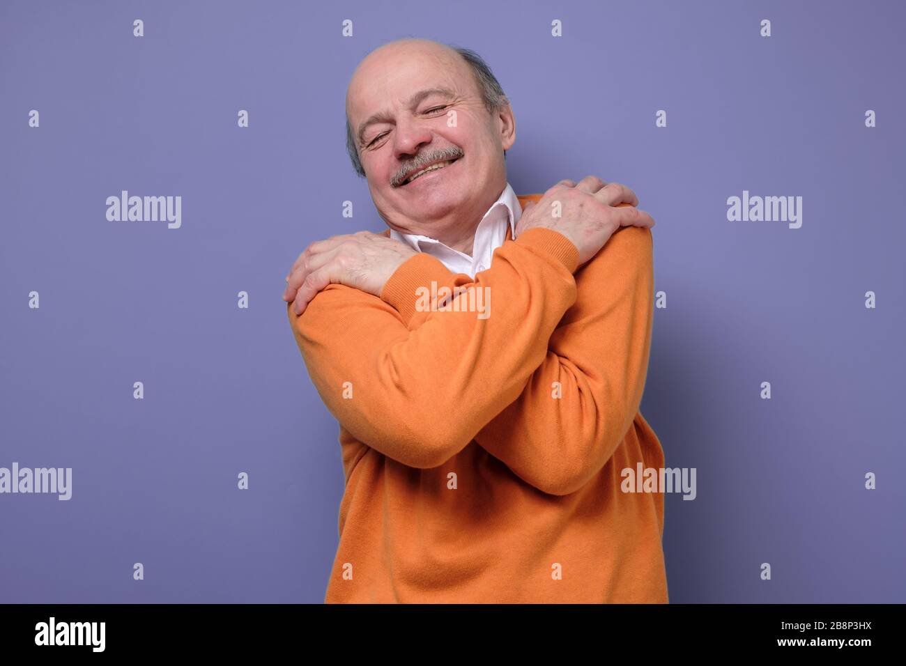 senior man hugs himself, has high self esteem feeling happy being alone. Stock Photo