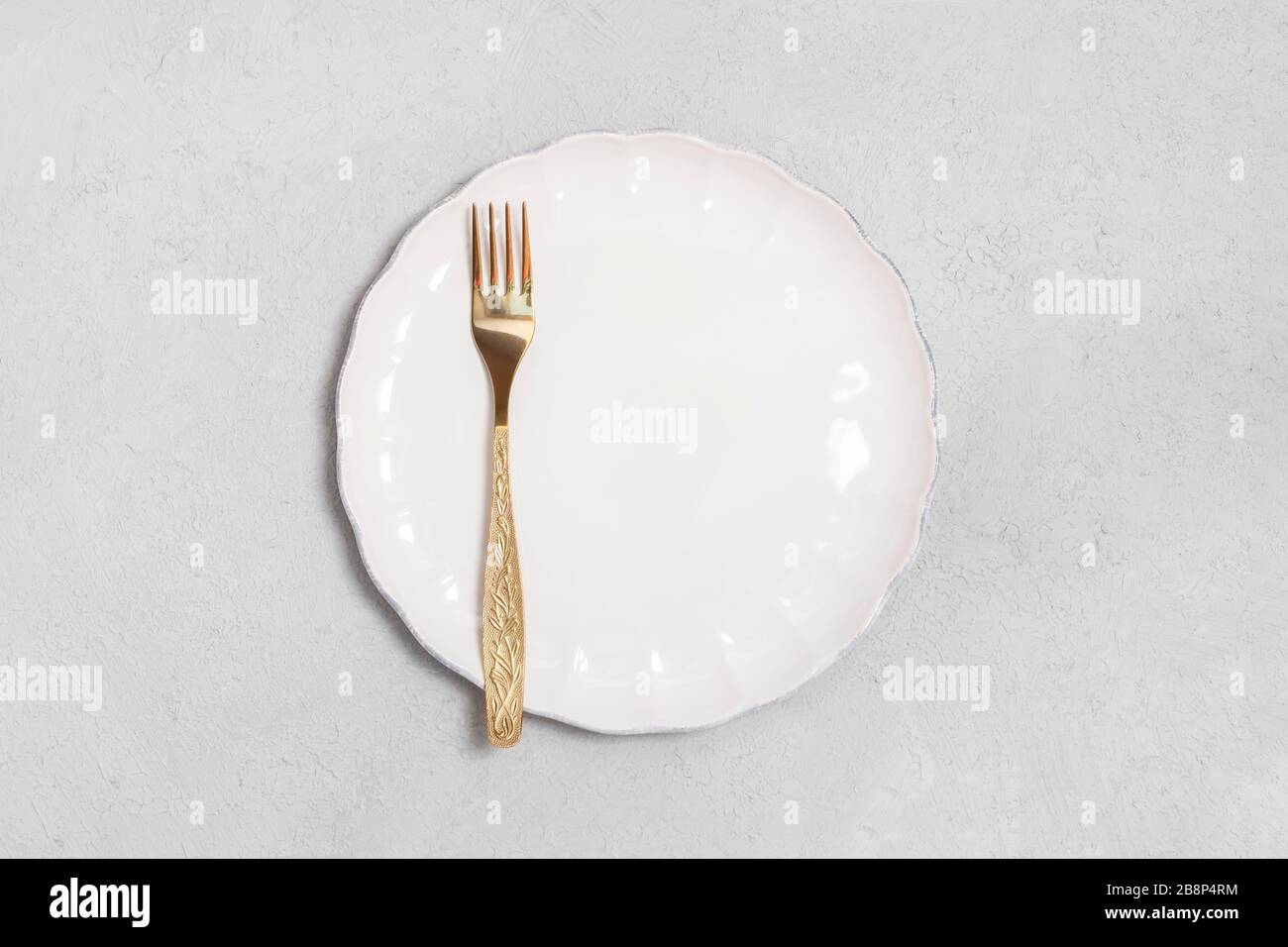 Directly above view of golden fork with white plate on neutral concrete background with space for text Stock Photo