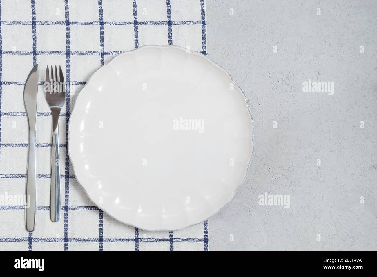 Empty white plate and silverware with napkin on neutral table background. Image with copy space, top view Stock Photo
