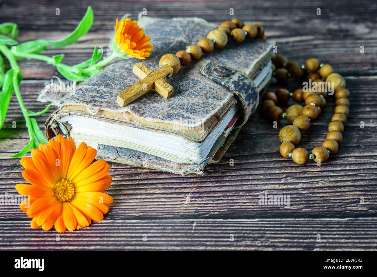 Wooden cross with chaplet on the ancient bible and a flower on the wooden background. Christian religion. We trust in god. Stock Photo