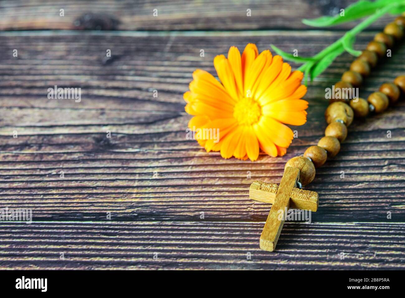 Christian cross with chaplet and flower on the wooden background closeup. Symbol of christian religion. Stock Photo