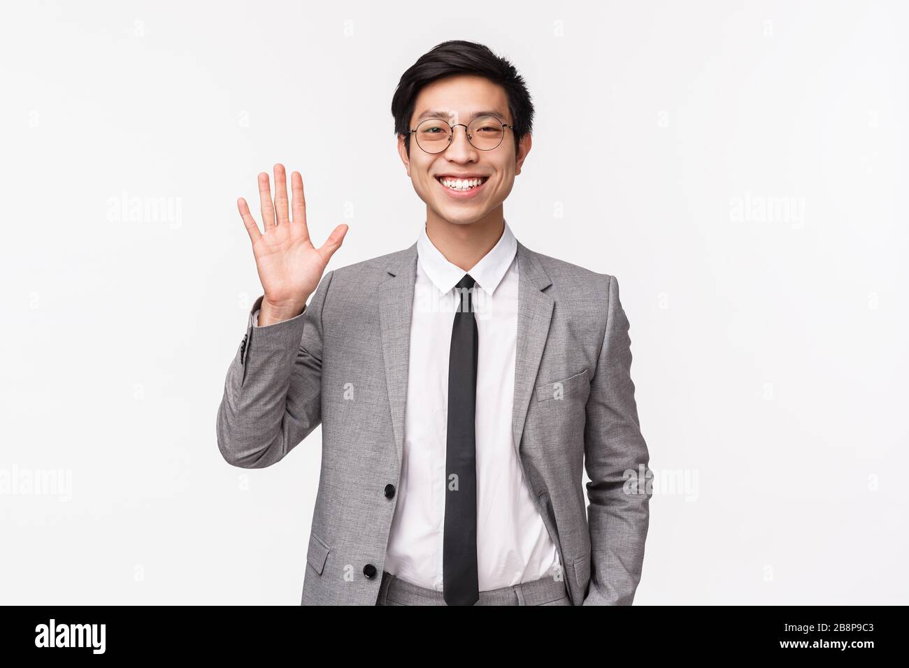 Waist-up portrait of friendly, cheerful smiling asian male entrepreneur, office worker saying hi, greeting coworker waving hand in hello, welcome Stock Photo