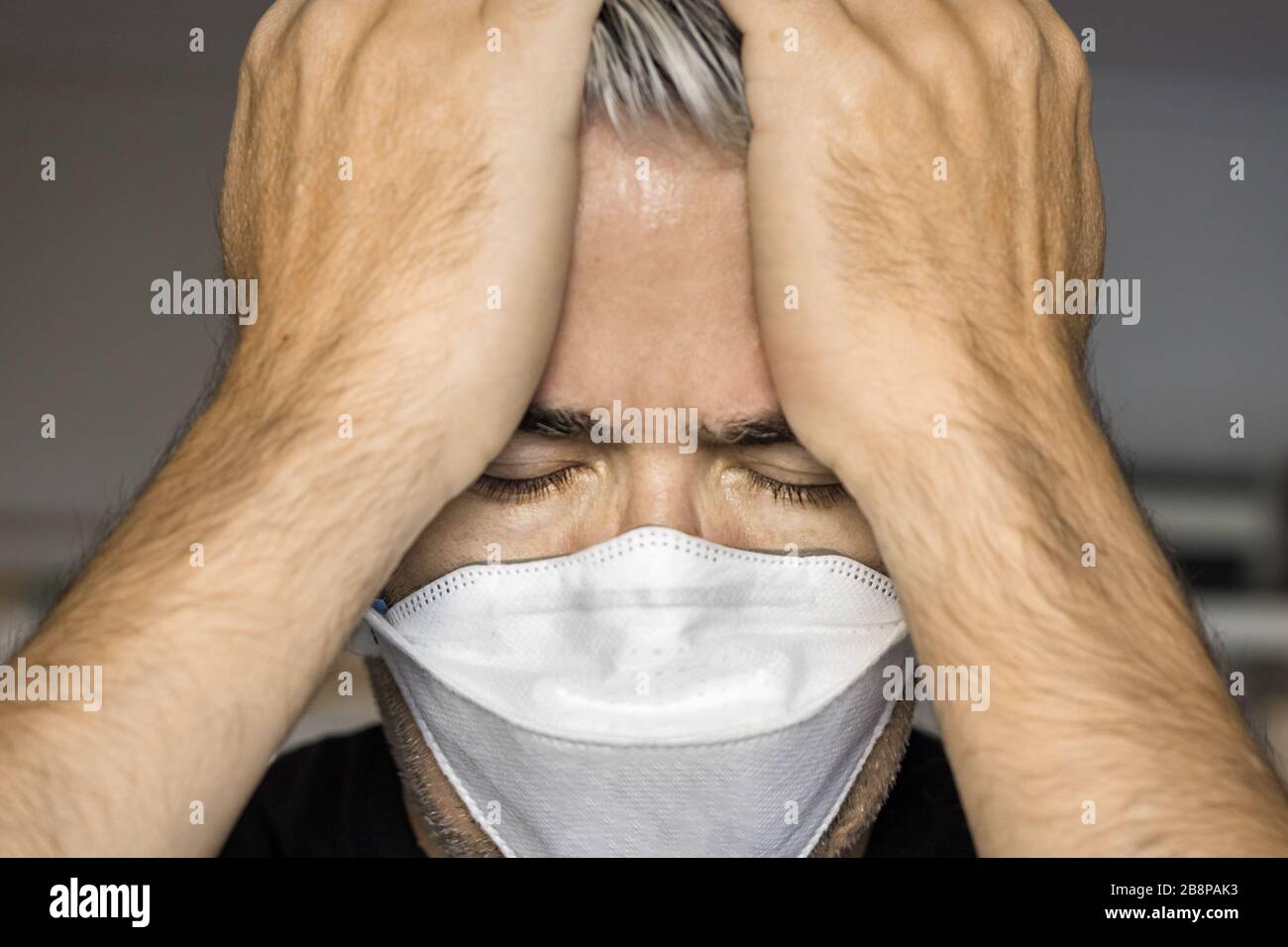 Portrait of a mature man wearing a protective mask with his hands on forehead, worry. Stock Photo