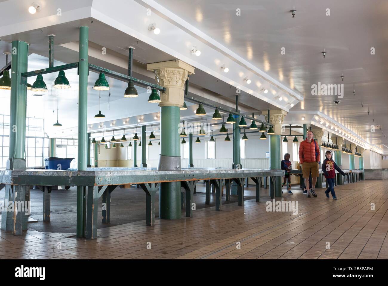 Visitors walk through an empty arcade at Pike Place Market on Sunday, March 22, 2020. While many of the food-related businesses are open, the landmark’s non-essential businesses are temporarily closed including the market’s ubiquitous souvenir and flower stalls. Stock Photo