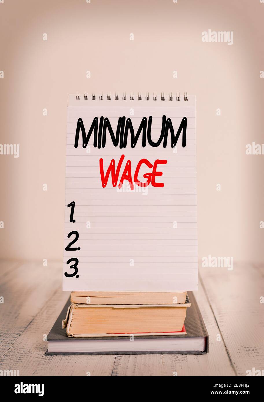 Conceptual hand writing showing Minimum Wage. Concept meaning the lowest wage permitted by law or by a special agreement Front view stacked books spir Stock Photo