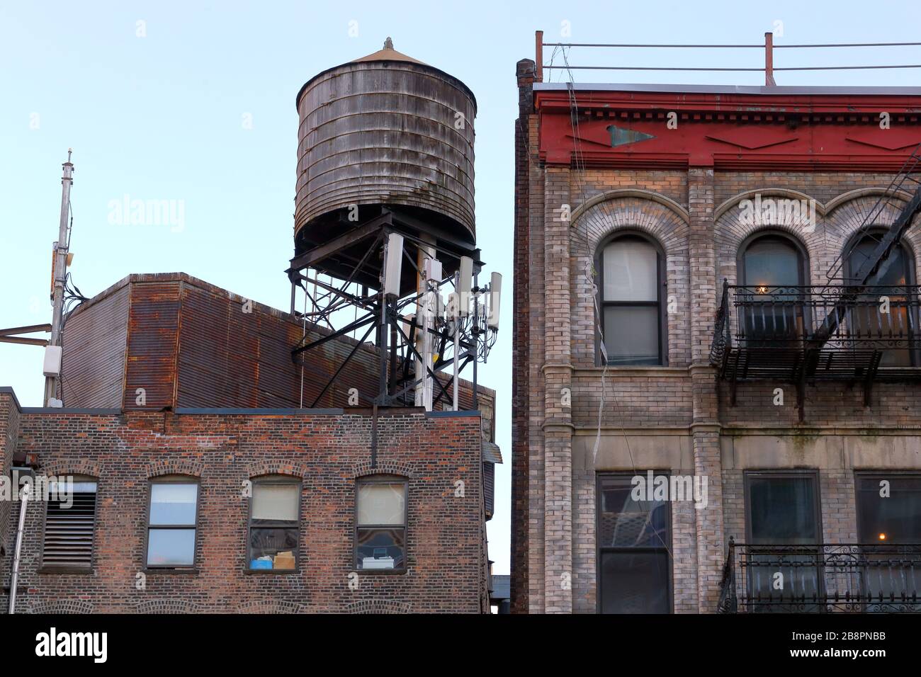 A wooden water tank on the roof of an industrial loft building next door to a tenement building in New York City Stock Photo