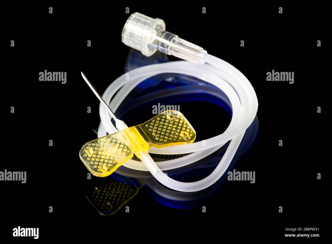 20 gauge yellow IV catheter and IV tubing on dark blue. Stock Photo