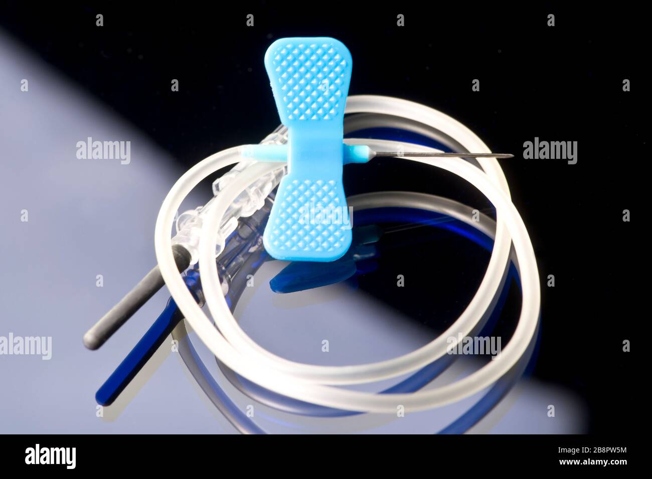 10 gauge blue IV catheter and IV tubing on dark blue background. Stock Photo