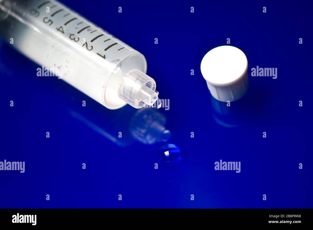 Pre-filled Sterile Saline injection vial droplet on blue reflective surface. Stock Photo