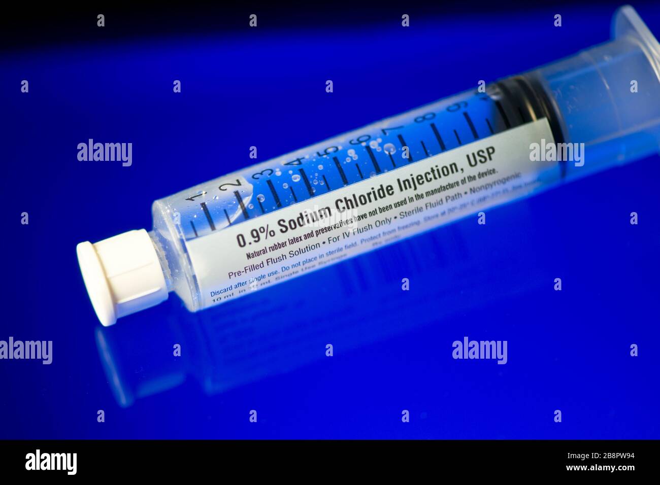 Close up of pre-filled sterile saline injection vial on blue reflective surface. Stock Photo