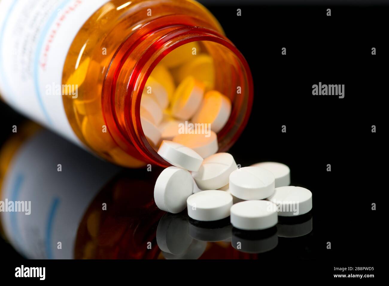 White tablets spill from prescription medicine bottle on black reflective surface. Stock Photo
