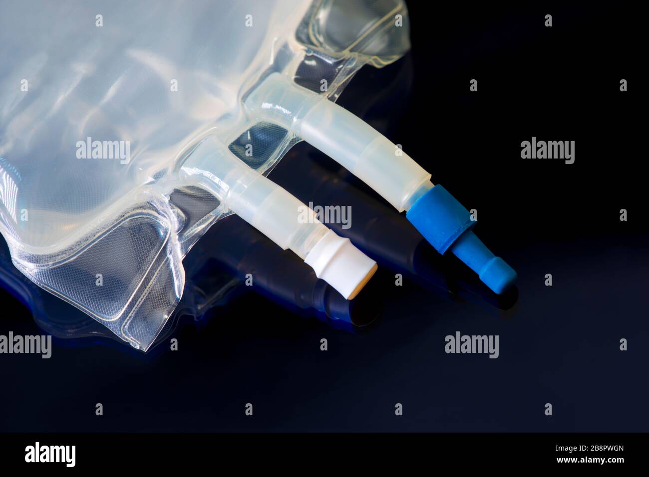 IV bag with medication ports and IV tubing on dark blue. Stock Photo