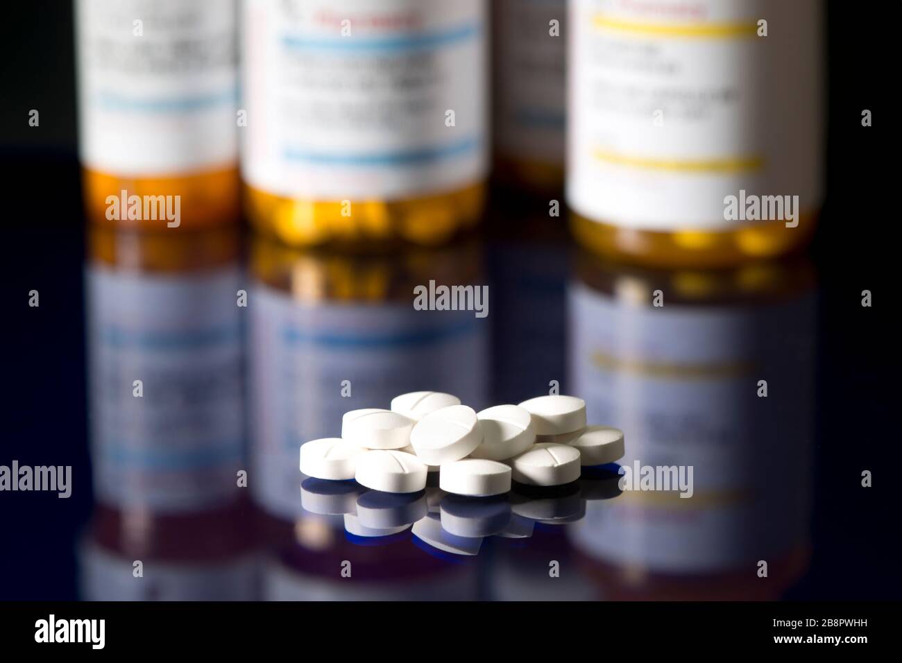 White tablets on dark reflective surface with prescription bottles in background. Stock Photo