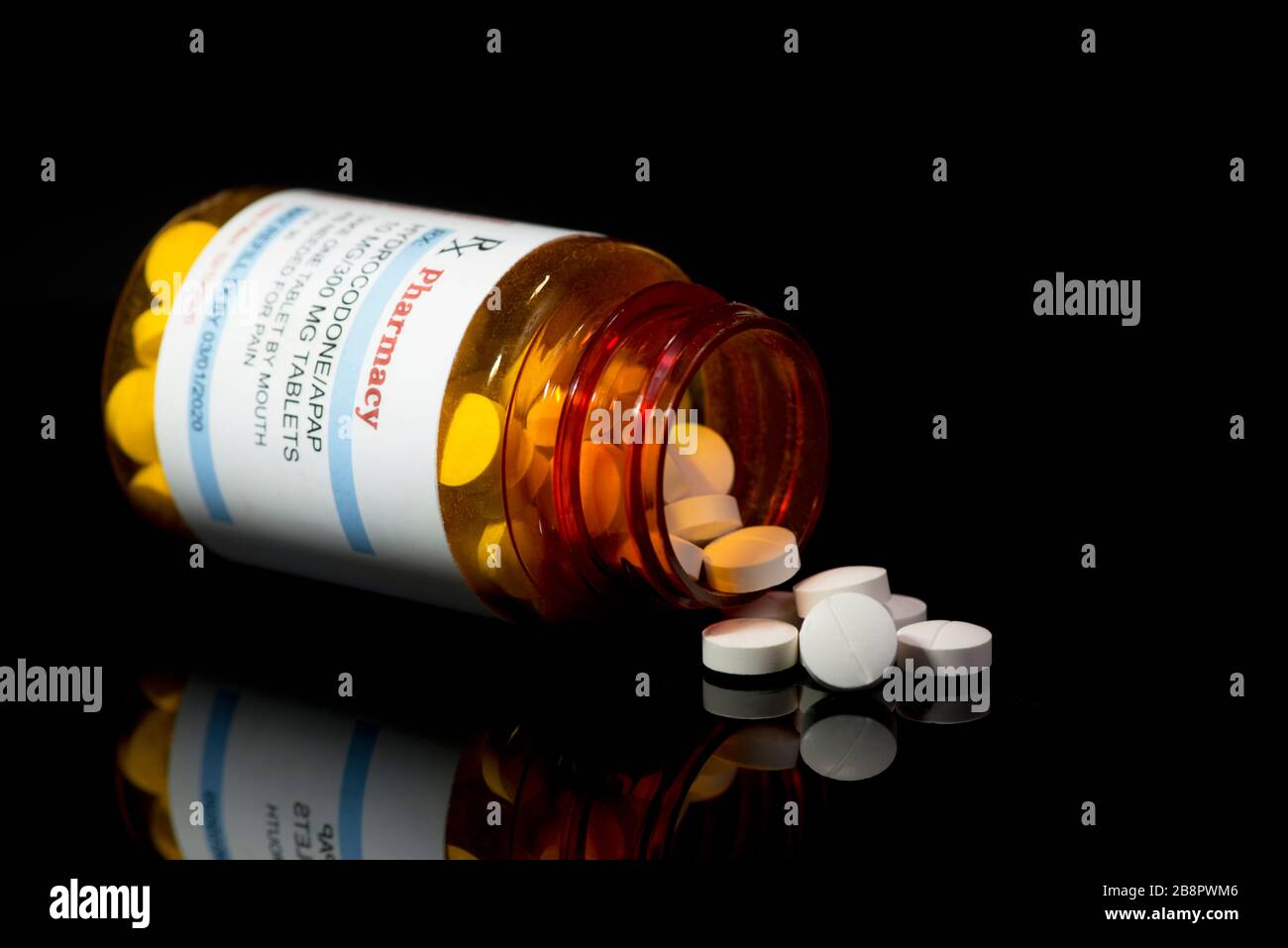 Hydrocodone/APAP acetaminophen prescription bottle with white tablets on black background. Stock Photo