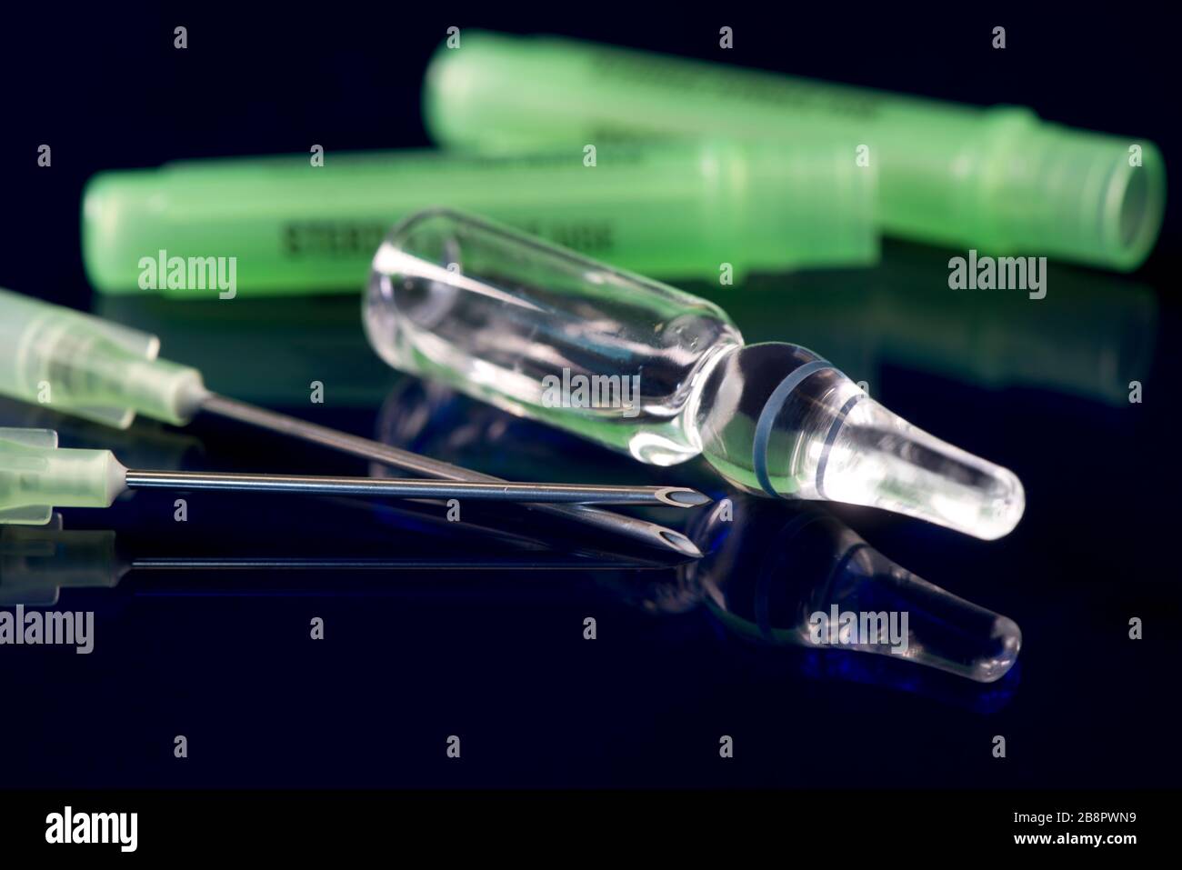 Clear glass medication ampule with two filter needles on blue reflective surface. Stock Photo