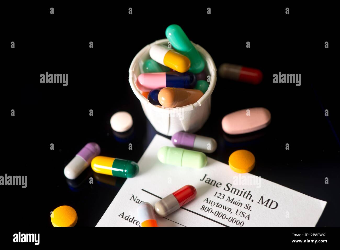 Many colored tablets and capsules with medication cup and doctor's prescription on dark background. Stock Photo