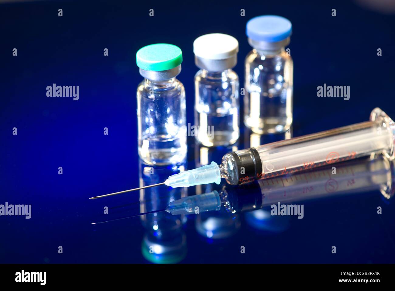 Syringe with three 5ml glass medication vials on blue reflective surface. Stock Photo