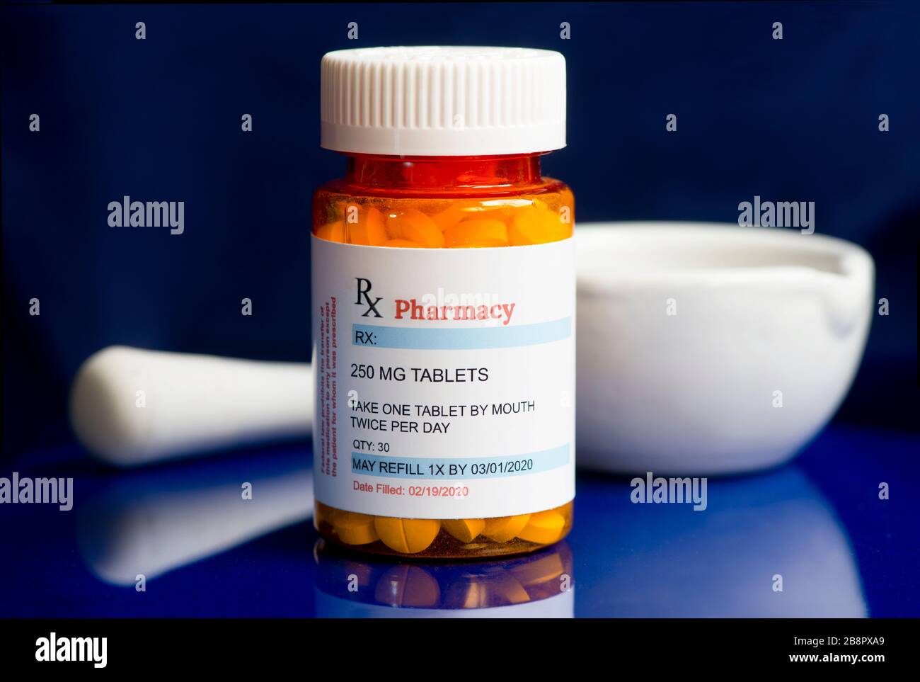 Generic prescription bottle with tablets and mortar and pestle on dark blue background. Stock Photo