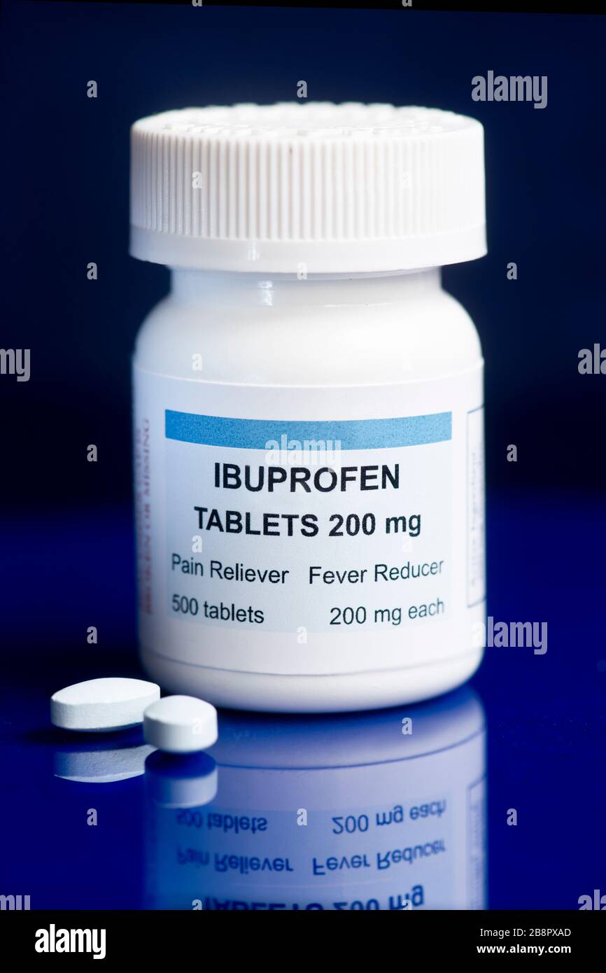 Ibuprofen container and two tablets on blue reflective surface. Stock Photo