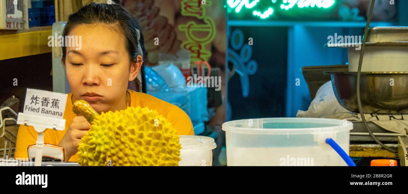 Woman sitting is a foodstall with a durian fruin on the counter in Jalan Alor Bukit Bintang Kuala Lumpur Malaysia. Stock Photo