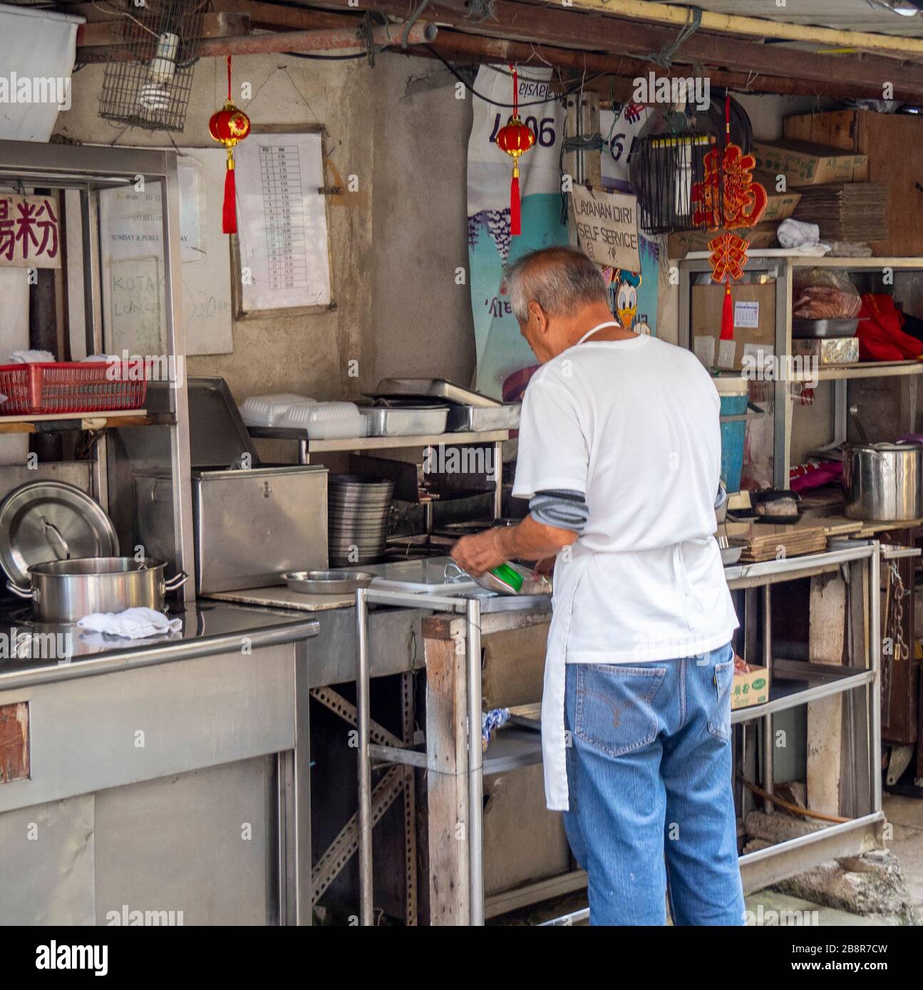 Male cook preparing food in outdoor kitchen of restaurant in laneway Lorong Panggung Chinatown City Centre Kuala Lumpur Malaysia. Stock Photo