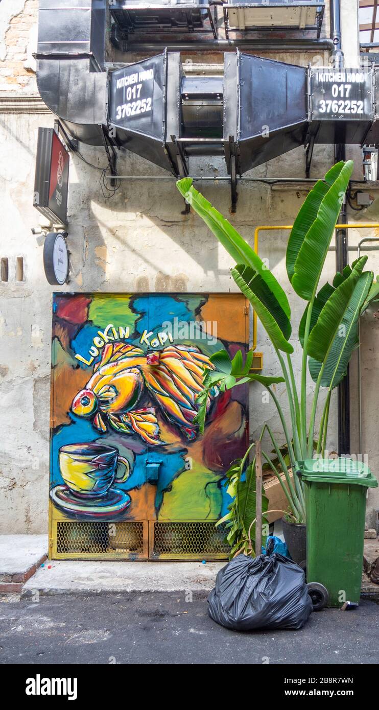 Rubbish bag wheelie bin and a pot plant beside street art on a metal cage in a laneway Lorong Panggung Chinatown City Centre  Kuala Lumpur Malaysia. Stock Photo
