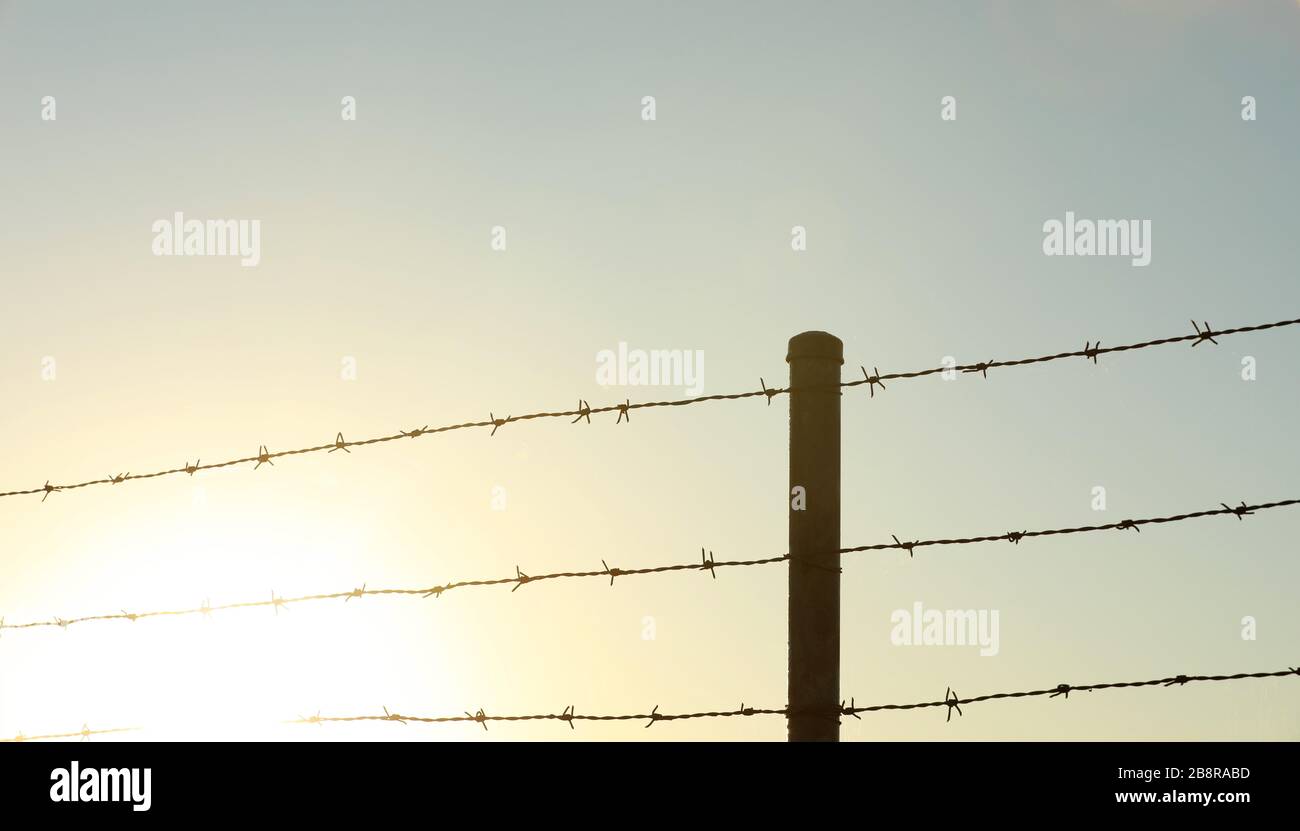 Sunrise burnt out in the corner. Barbed barb wire fences and fence post. suggestion of hope and positivity Stock Photo