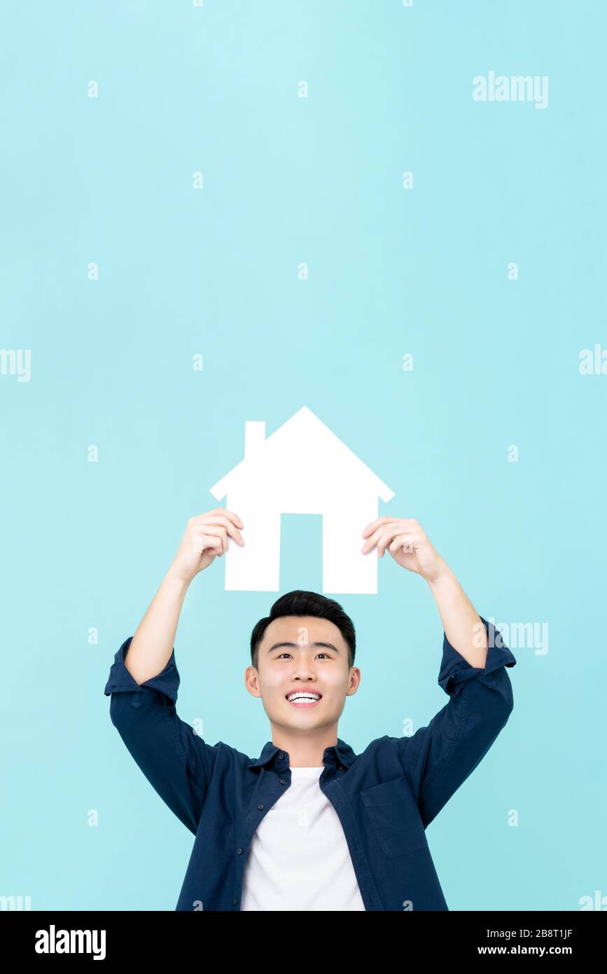 Happy young Asian man holding house sign with copy space  overhead isolated on light blue background for real estate concepts Stock Photo
