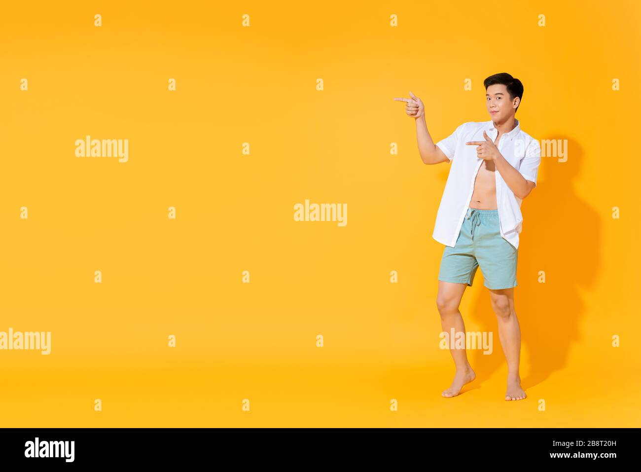 Full body of young handsome Asian man in casual summer outfit pointing hands to copy space aside on colorful yellow background Stock Photo