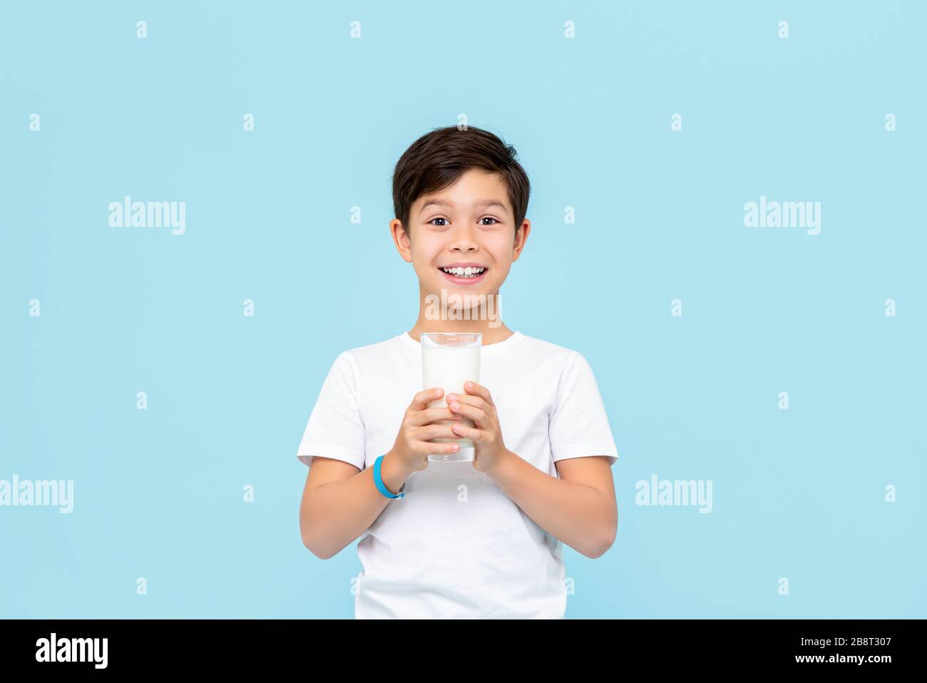 Happy smiling Mixed race boy drinking fresh milk isolated on light blue studio background Stock Photo