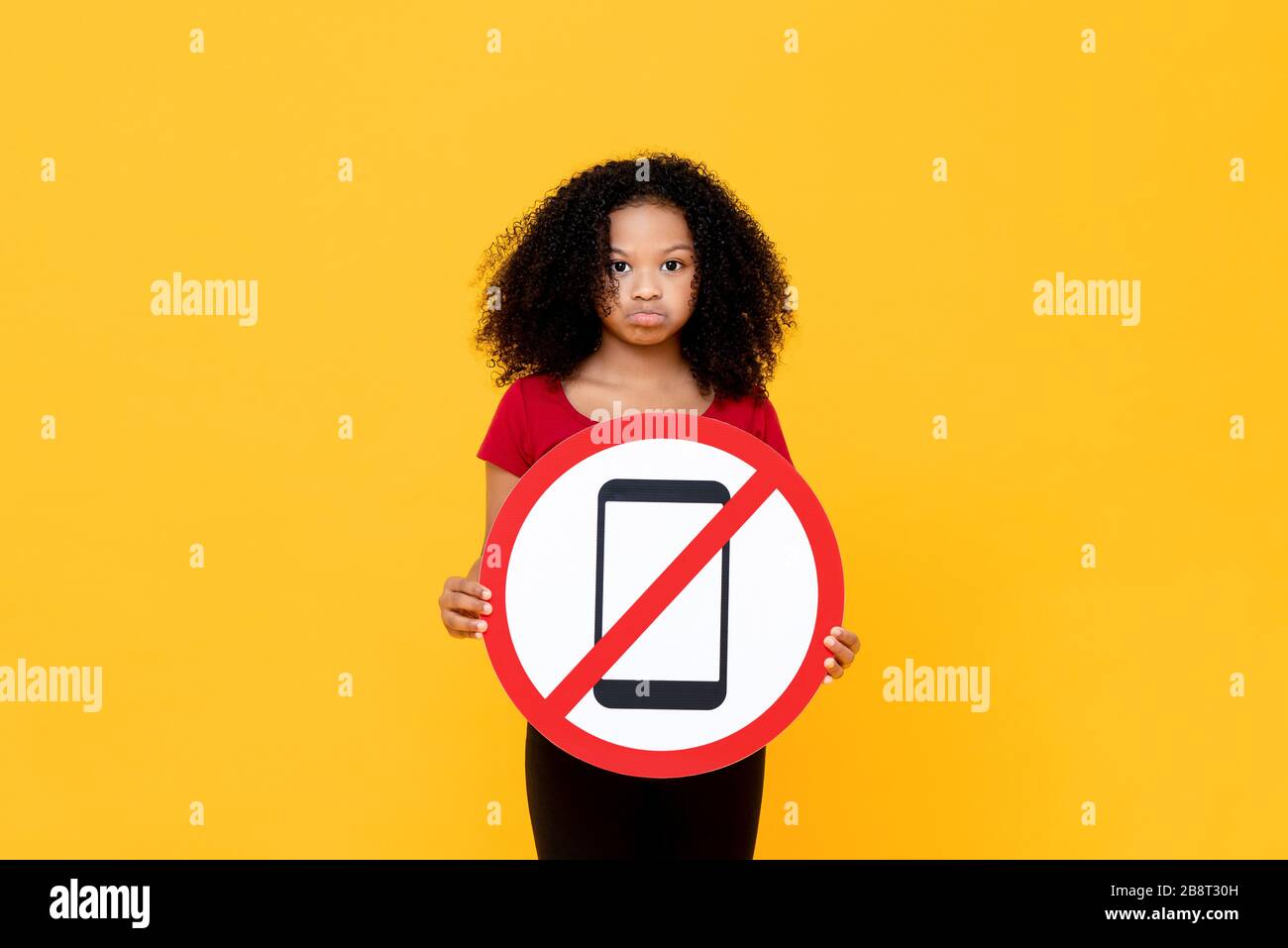 Mixed race African girl showing no mobile phone usage sign isolated on colorful yellow background Stock Photo