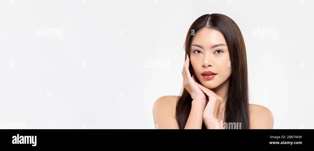 Banner beauty shot of confident Asian woman model with clear fair skin doing hands touching face pose in white isolated studio background with copy sp Stock Photo